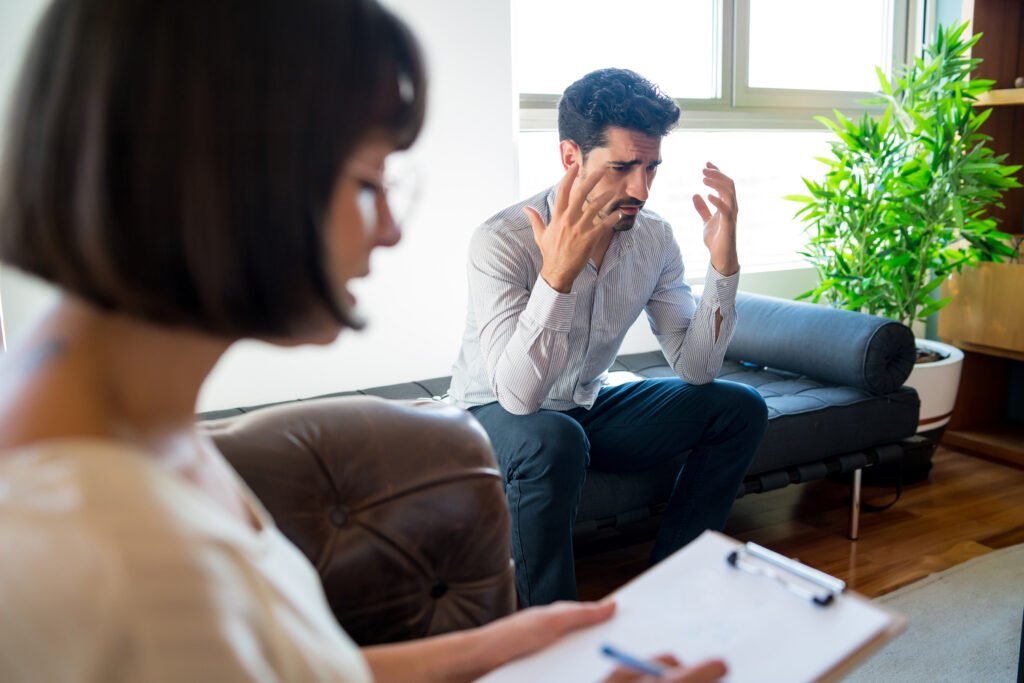 Anxious man speaking with a therapist during a counseling session about stress, emotional overload, and hidden anxiety symptoms