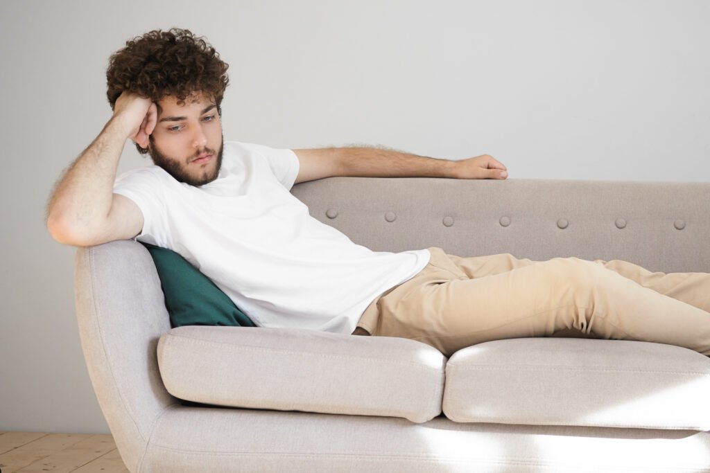 Man lying on couch feeling drained and unmotivated, illustrating one of the signs you need depression therapy